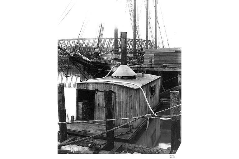 A wooden structure on a dock with a steamship in the background, likely from the late 19th or early 20th century.