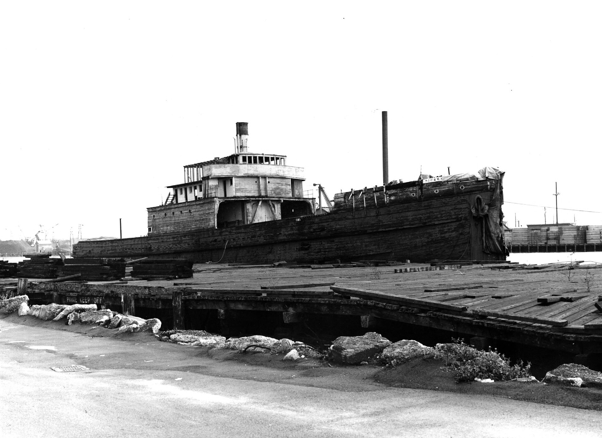 A wooden ship docked at a shipyard with a partially covered structure, possibly undergoing maintenance or repair.